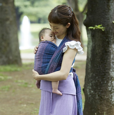 女性が赤ちゃんをベビーラップで抱っこし立っている写真