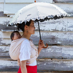 眠る赤ちゃんをベビーラップでおんぶして日傘をさす女性