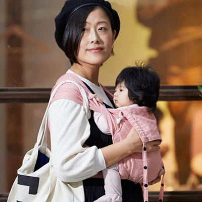 ピンク色の抱っこ紐で赤ちゃんを抱っこする日本人女性