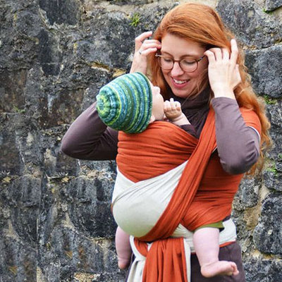 コッパ―色のストレッチラップで子どもを抱っこする女性