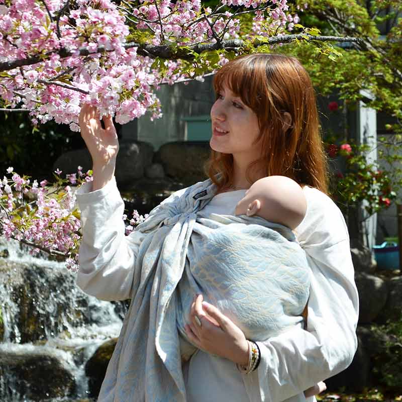優しいパステルブルーのスリングで赤ちゃん人形を抱っこしほほ笑む女性