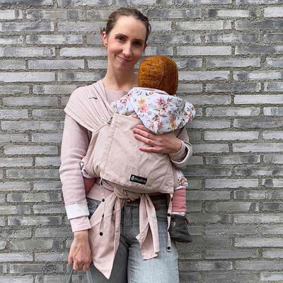 ピンクベージュの抱っこ紐で赤ちゃんを抱っこしてほほ笑む女性