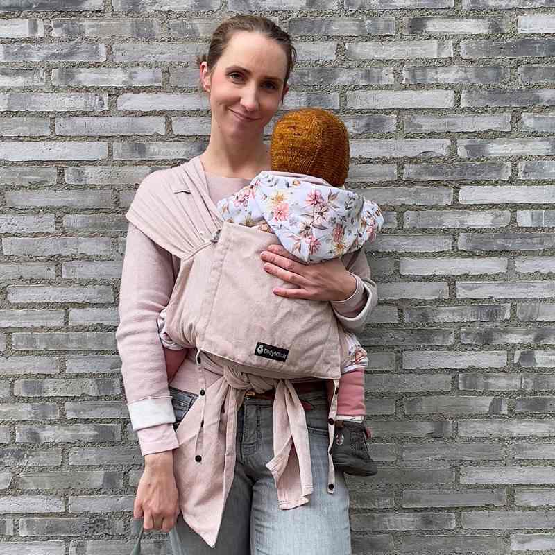 ピンクベージュの抱っこ紐で赤ちゃんを抱っこしてほほ笑む女性