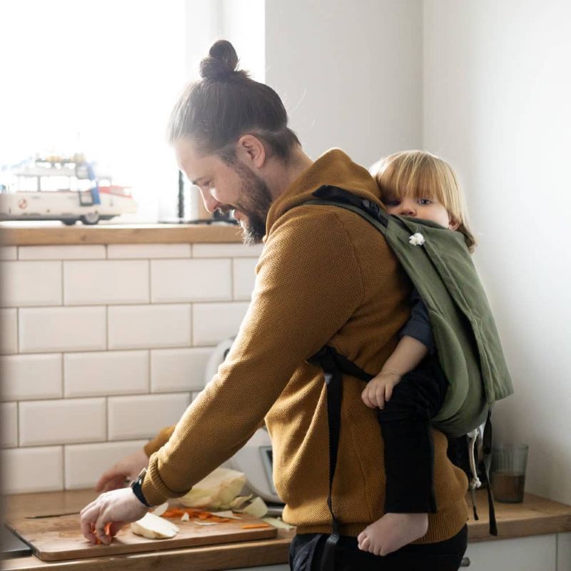 オリーブ色のおんぶ紐で子供をおんぶして料理をする男性