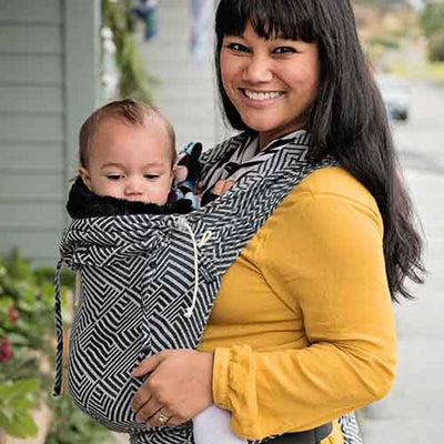 黄色い服を着た女性がモノトーンの抱っこ紐で赤ちゃんを抱っこしている様子