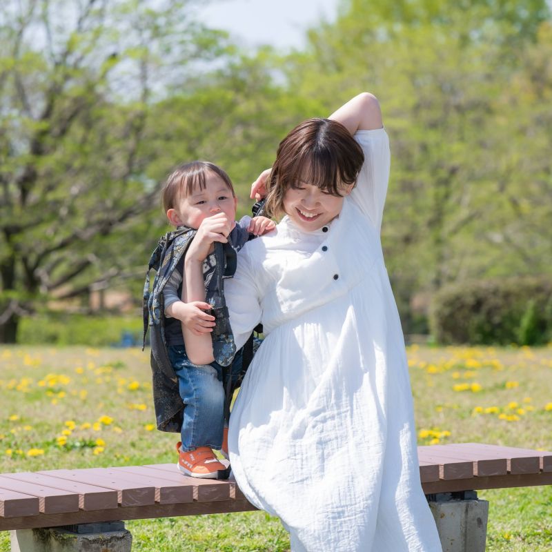 ベンチに座っている妊婦さんがおんぶ紐で息子を負ぶいあげている瞬間