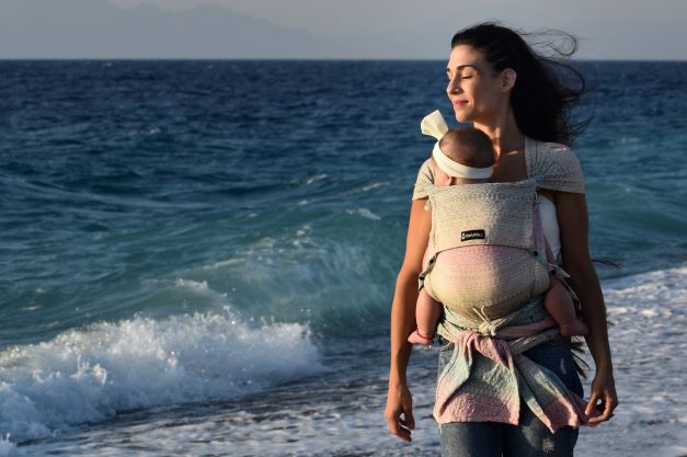 抱っこ紐で海辺を歩くギリシャの女性