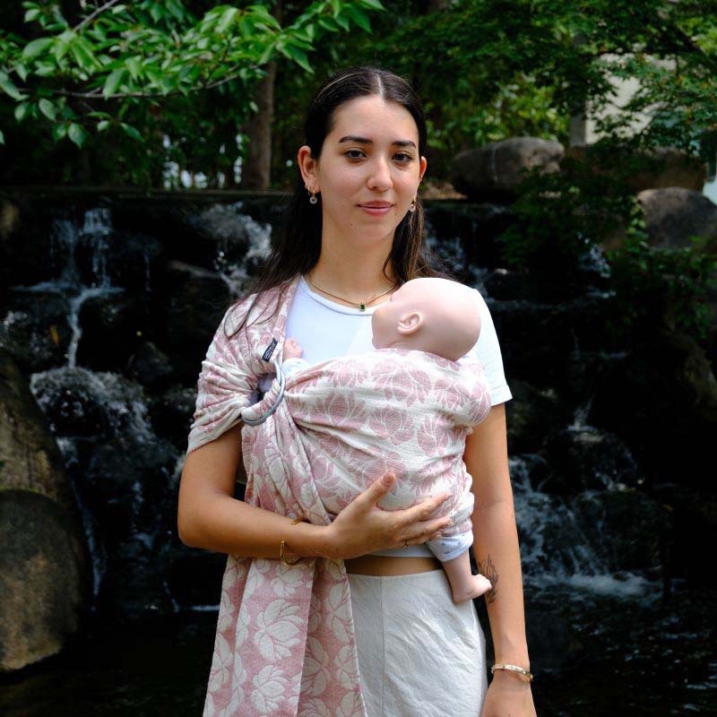 蓮柄のリングスリングで赤ちゃん人形を抱っこする若い女性