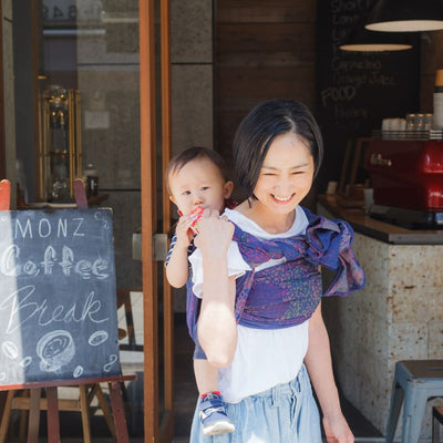 紫色のベビーラップで男の子をおんぶしながら喫茶店から出るお母さん