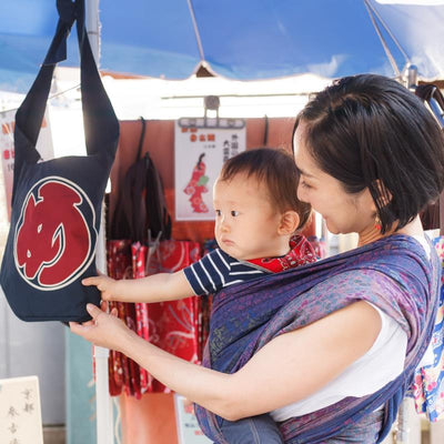 アジサイ模様のベビーラップで子どもを抱っこしながら和柄のバッグを眺めているお母さん