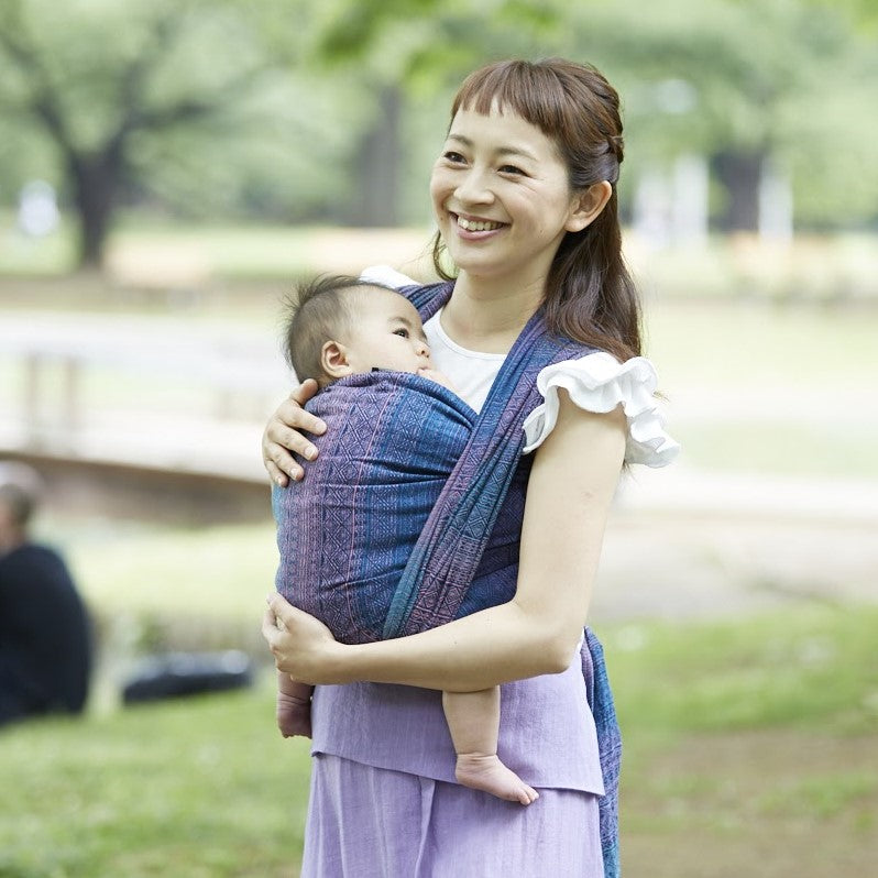 女性が赤ちゃんをベビーラップで抱っこし、笑顔の写真