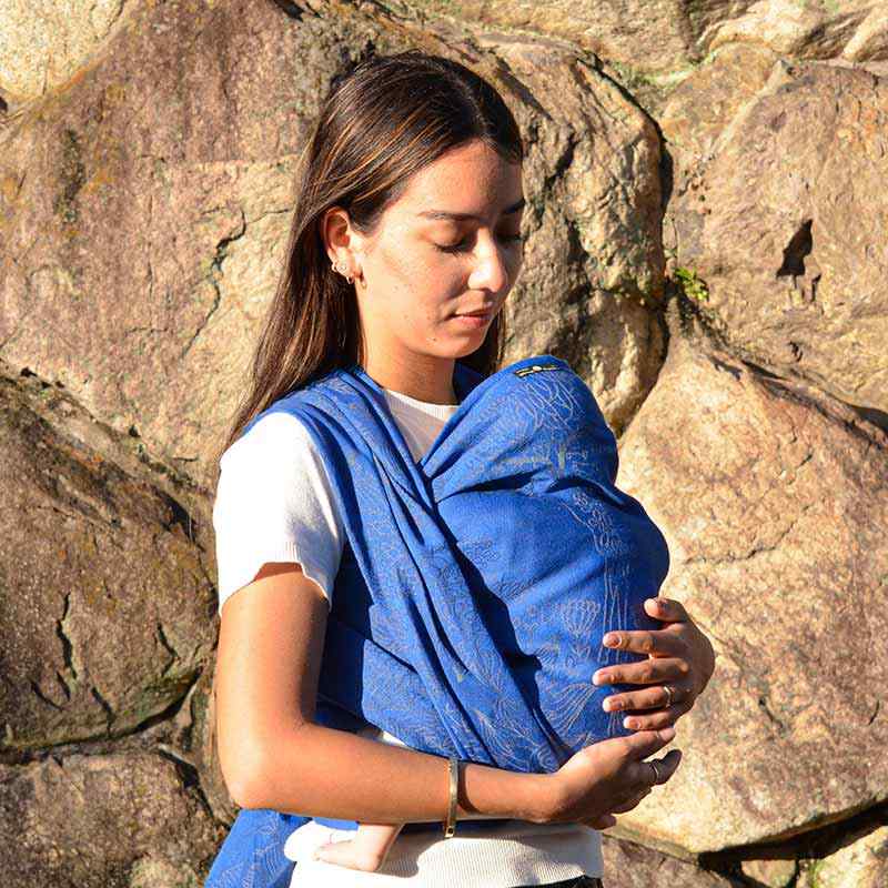 きれいなブルーのベビーラップで赤ちゃんを抱っこする女性
