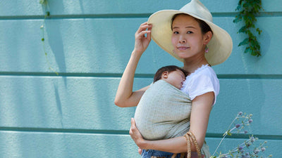 夏に赤ちゃんをミント色のベビーラップで抱っこする女性