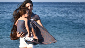スリングで幼児を抱っこし、地中海の海岸で散歩するお母さん