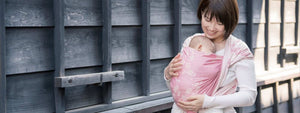 桜柄のラップで首すわり前の赤ちゃんを抱っこする女性