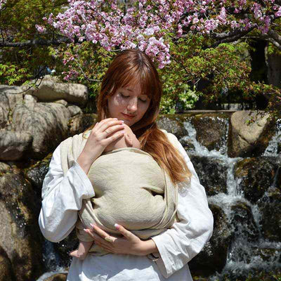 新芽のような淡いパステルグリーンのベビーラップで赤ちゃん人形を抱っこする女性