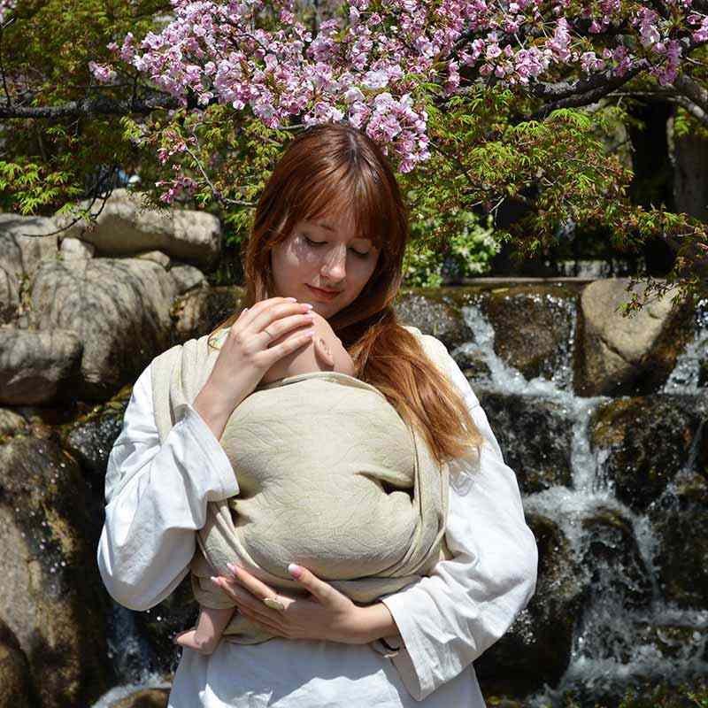 新芽のような淡いパステルグリーンのベビーラップで赤ちゃん人形を抱っこする女性