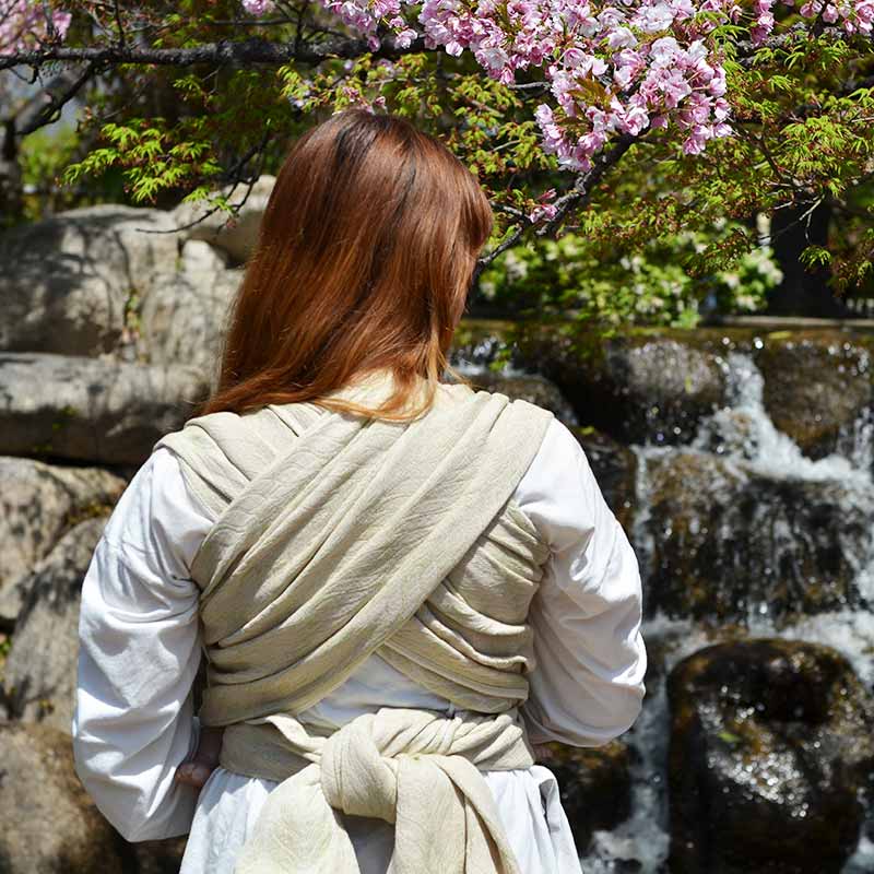 新芽のような優しいパステルグリーンのベビーラップで赤ちゃん人形を抱っこする女性の後ろ姿