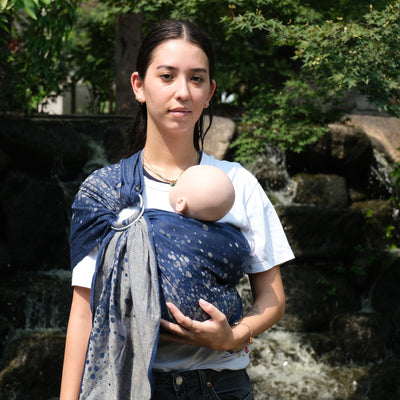 紺地にシルバーの玉模様がランダムに散りばめられたスリングで赤ちゃん人形を抱っこする女性