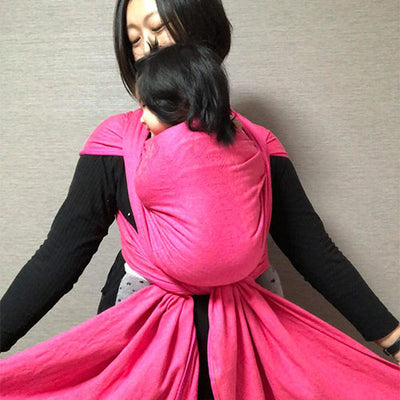 鮮やかなピンクのベビーラップで子供を抱っこする女性