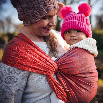 赤いベビーラップで子供を抱くニット帽の女性