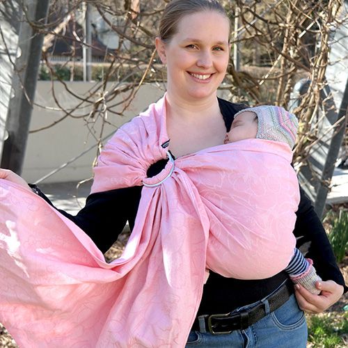 ピンク色のスリングで眠る赤ちゃんを抱っこする女性
