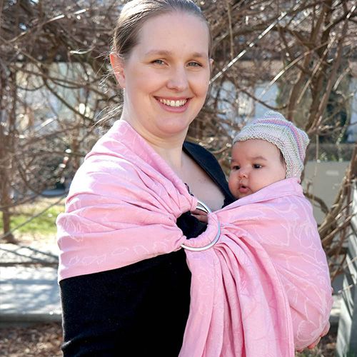 ピンク色のスリングでニット帽をかぶる赤ちゃんを抱っこしている白人女性