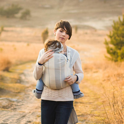 グレーの抱っこ紐で赤ちゃんを抱っこしながら散歩する女性