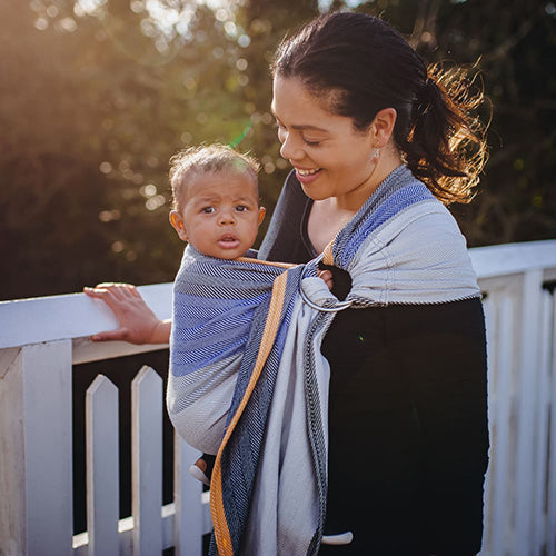 青、白、黒、オレンジのストライプ柄のスリングで赤ちゃんを抱っこする女性