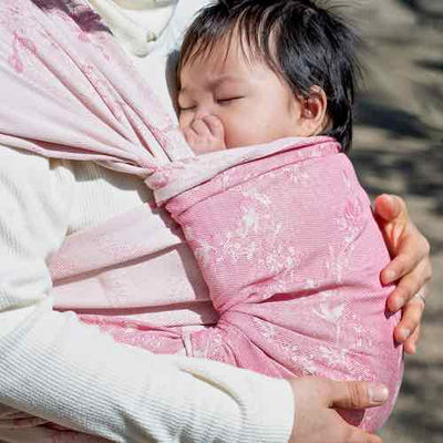 ピンク色のベビーラップで抱かれて寝ている赤ちゃん