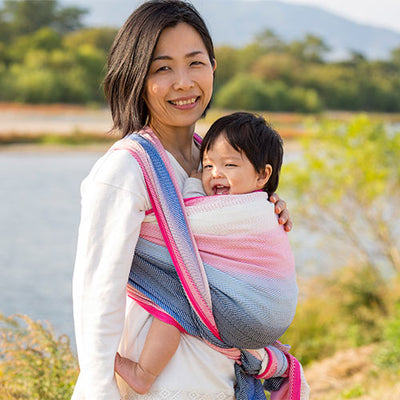 ブルーとピンクのベビーラップで赤ちゃんを抱っこする女性