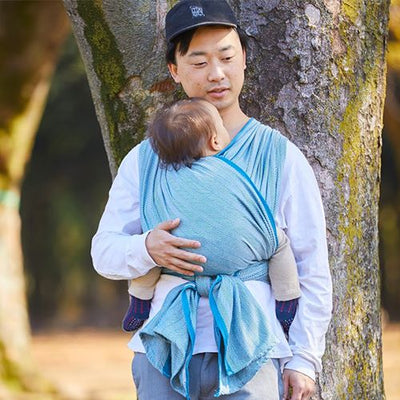 木の前でベビーラップで子供を抱き立っている男性