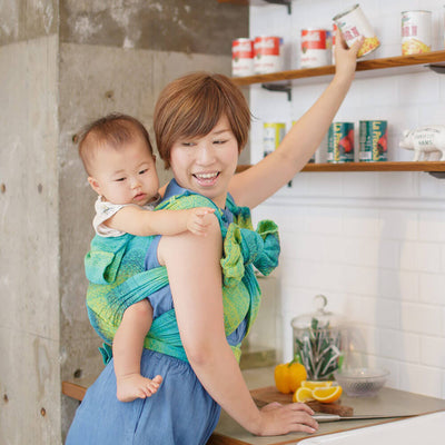 料理するお母さんに抱っこ紐でおんぶされる赤ちゃん