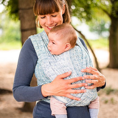 青い抱っこ紐で赤ちゃんを抱っこして、嬉しそうな表情をしている女性