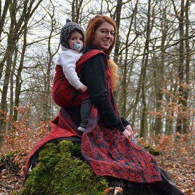 森の中で赤い抱っこ紐で子供を高くおぶる女性