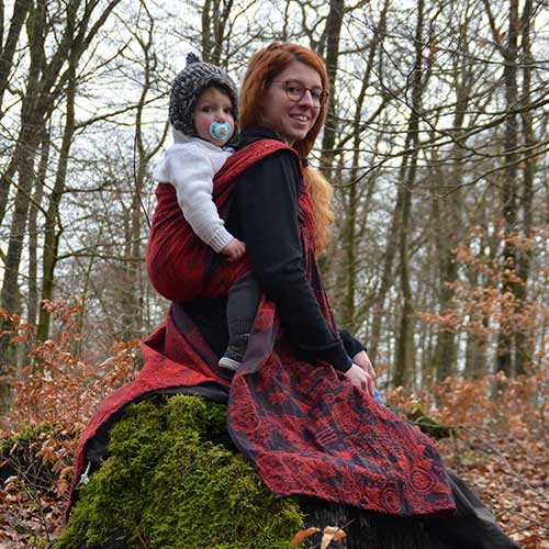 森の中で赤い抱っこ紐で子供を高くおぶる女性