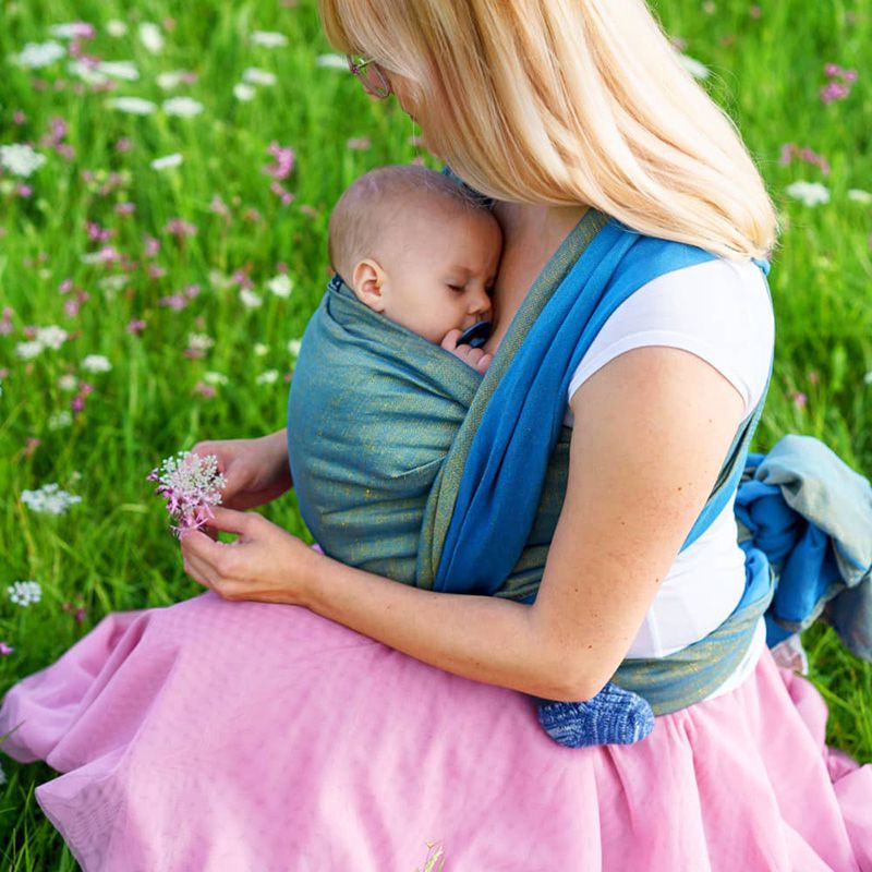 ブルーの抱っこ紐で赤ちゃんを抱っこしながら花を摘む金髪の女性
