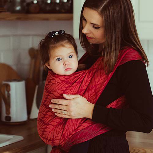 赤い抱っ子紐で赤ちゃんを抱っこする女性